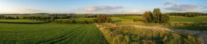Skup działek w górach - rozległe zielone pola uprawne z widokiem na małą wioskę w tle.